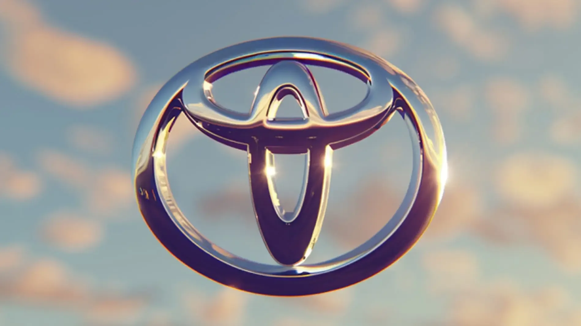 Toyota logo in front of a soft cloudy sky, lit by the sunset